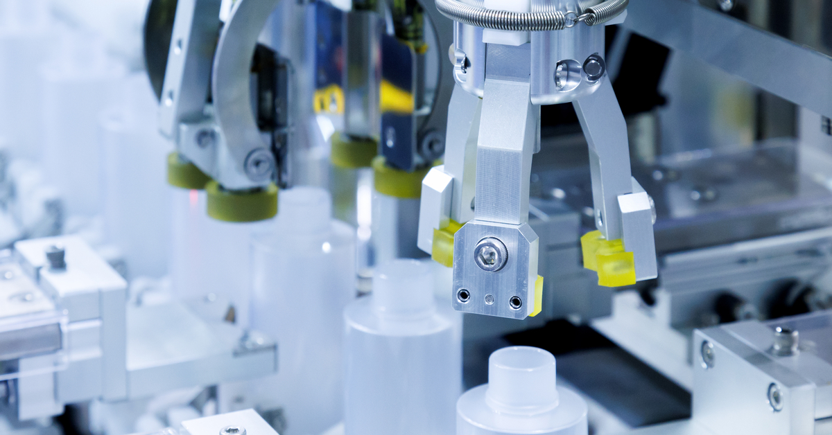 A machine with a metal arm operating over a row of plastic bottles moving down and assembly line in a factory.