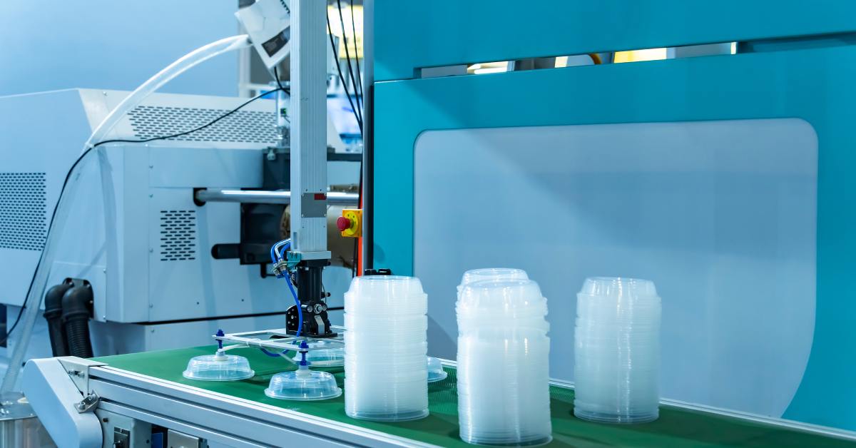 A close-up of a stack of polypropylene food containers on the conveyor belt of a plastic injection molding machine.